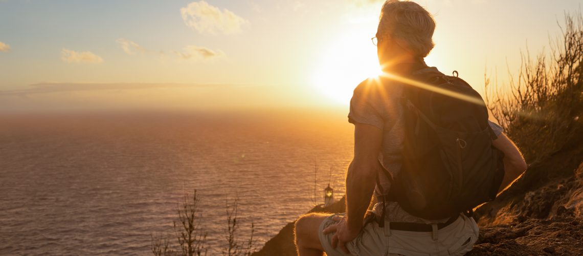 Mature man hiker watching sunrise from mountain top.
