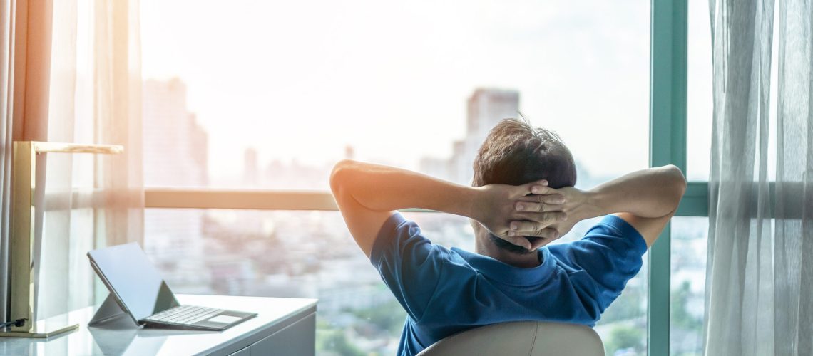 Life-work balance and city living lifestyle concept of business man relaxing, take it easy in office or hotel room resting with thoughtful mind thinking of life quality looking forward to cityscape